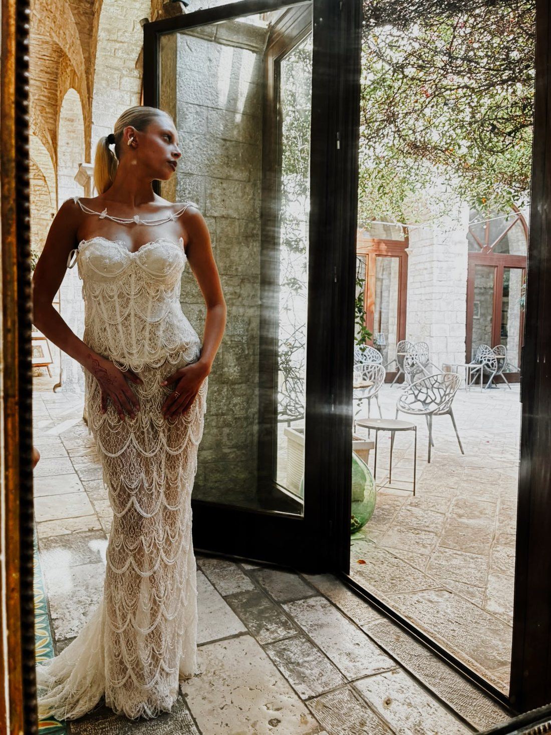 Abito da sposa lungo in pizzo a festoni, sulla soglia di un chiostro in pietra