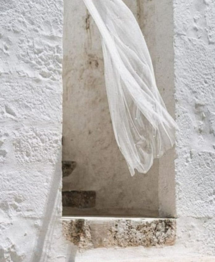 Velo da sposa bianco che vola in una finestra di pietra imbiancata a calce